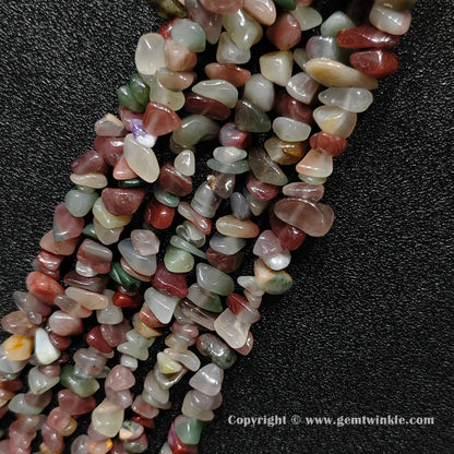 Angled view of tumbled purple and green agate freeform chip gemstone strands