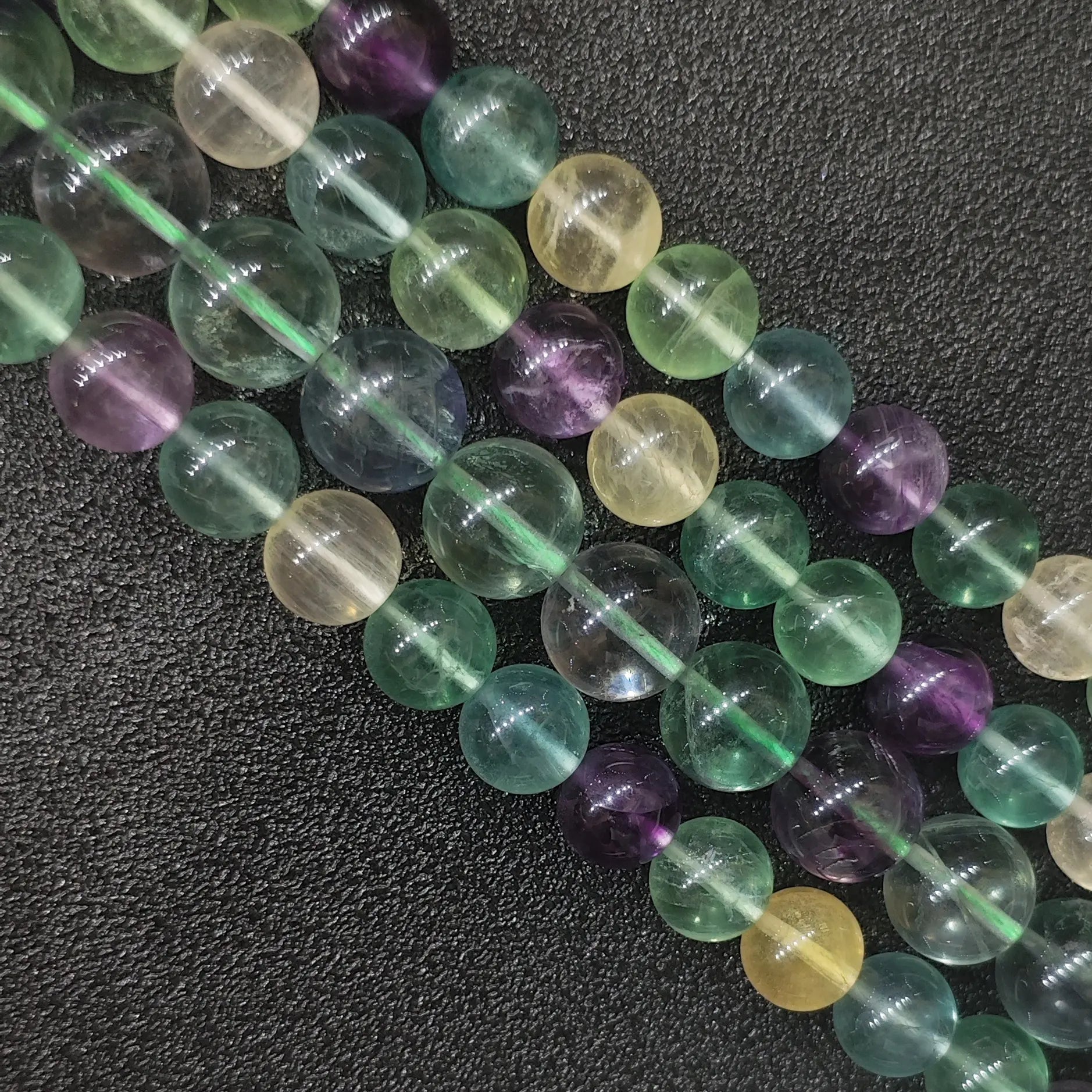 Grade AB natural rainbow fluorite round loose beads strands with mixed purple green and yellow colors showing subtle ice cracks and inclusions on a dark background