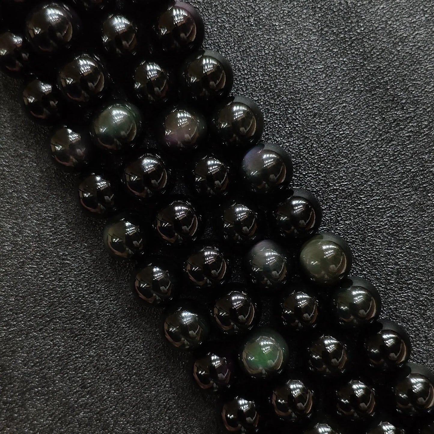 Natural rainbow obsidian crystal beads showing vibrant green and purple iridescent eyes on dark round strands