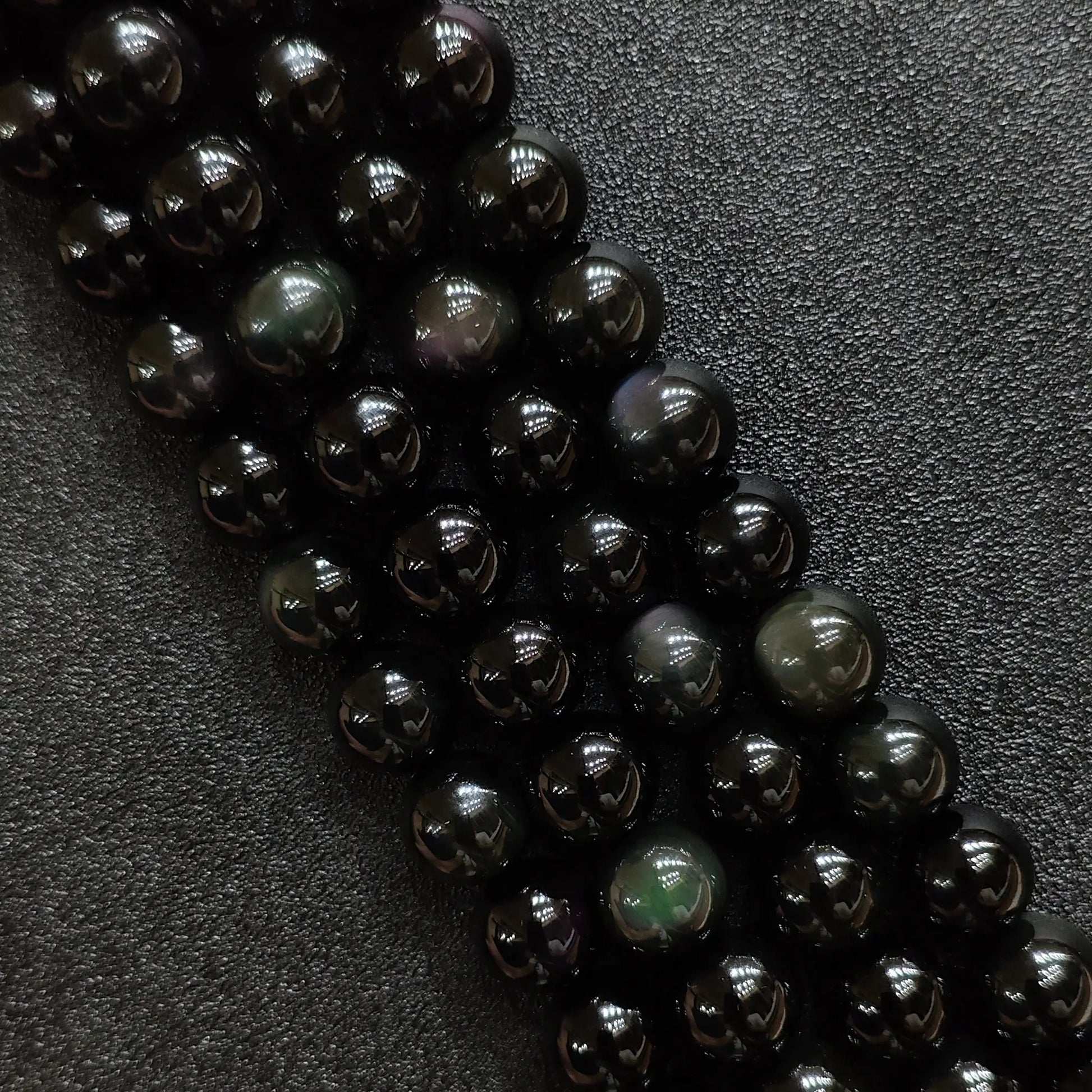 Natural rainbow obsidian crystal beads showing vibrant green and purple iridescent eyes on dark round strands