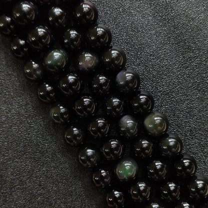 Natural rainbow obsidian crystal beads showing vibrant green and purple iridescent eyes on dark round strands