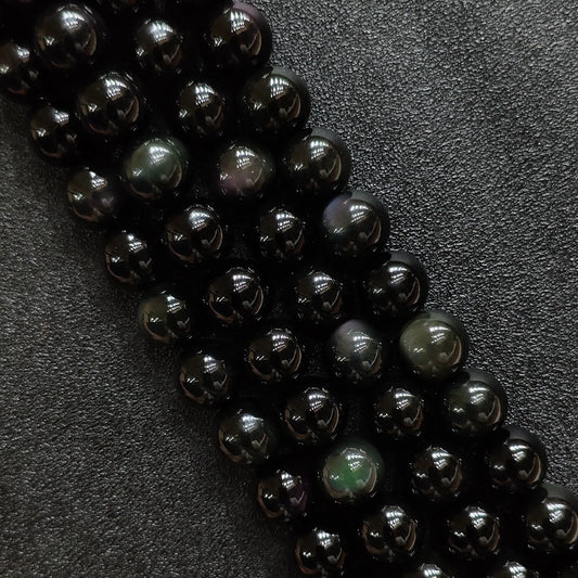 Natural rainbow obsidian crystal beads showing vibrant green and purple iridescent eyes on dark round strands