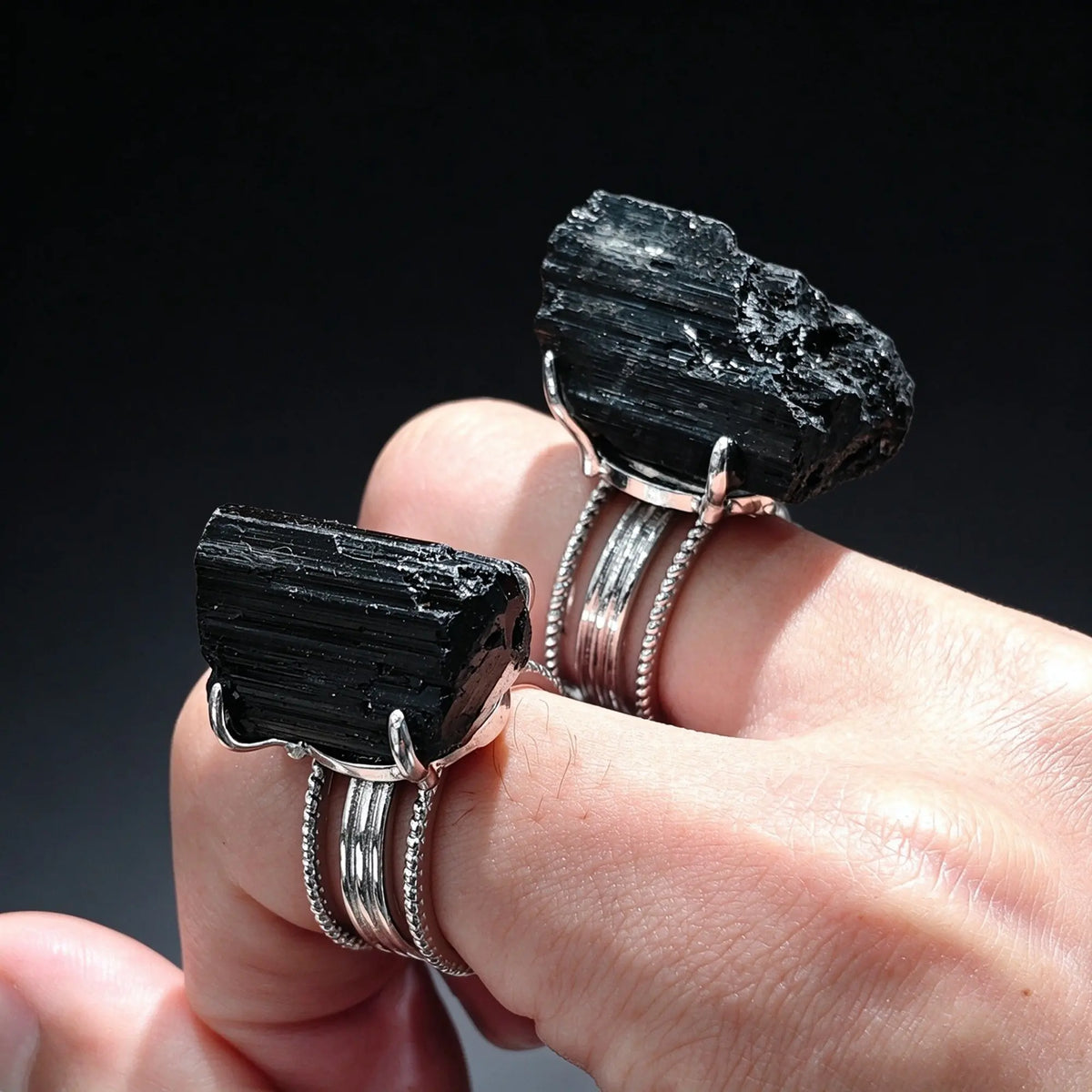 Hand wearing two natural raw black tourmaline rings in silver prong settings displaying hand trimmed crystal nuggets