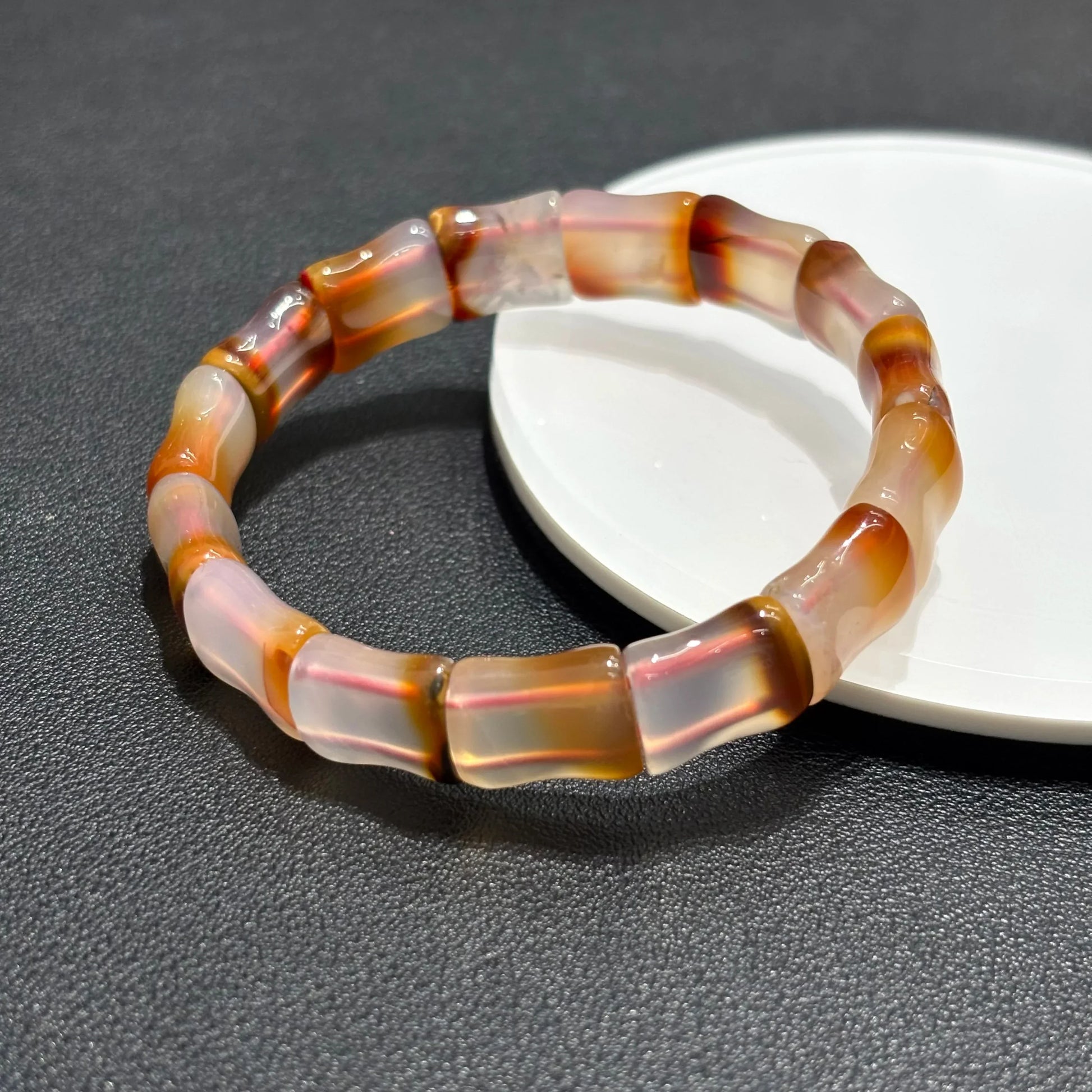 Single Natural Red Agate Bangle Bracelet resting on a white plate, showing the bamboo bead shape and warm red-brown hues.
