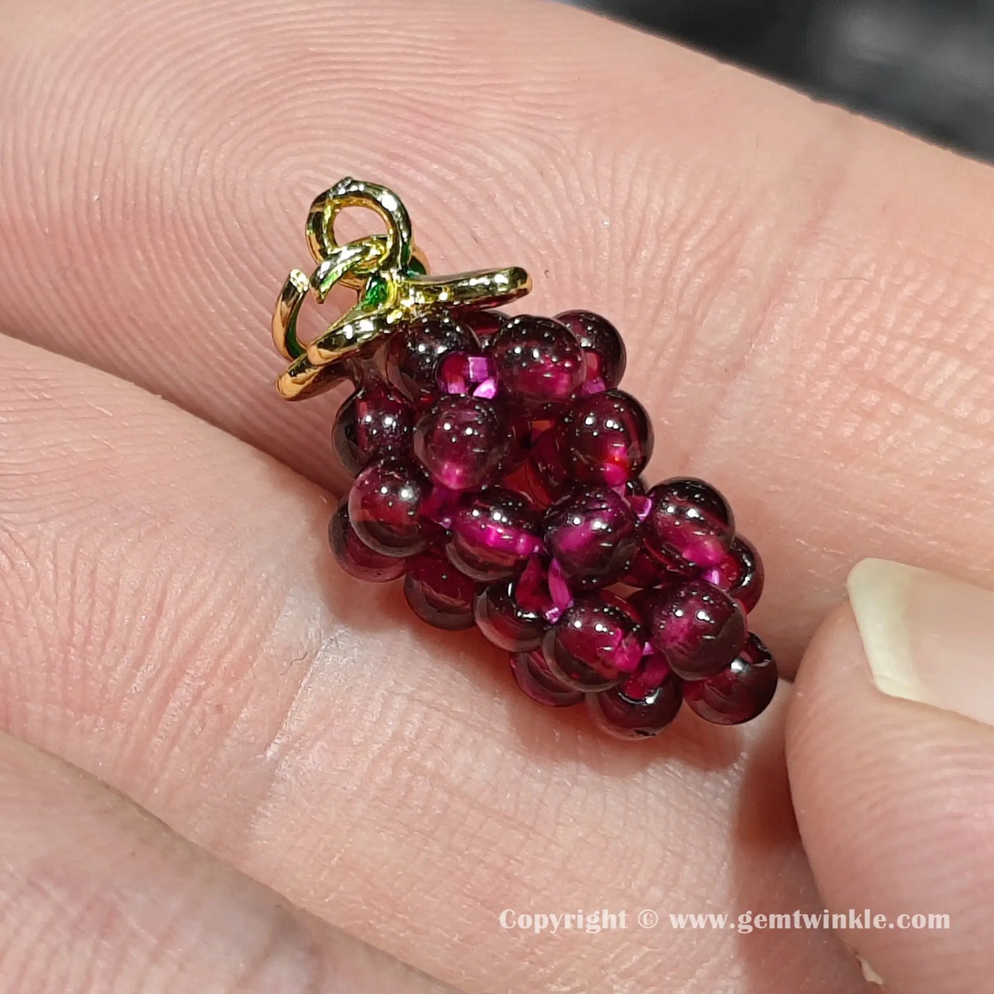 Close up details of natural red garnet cluster grape bead displaying translucent rich tones on finger