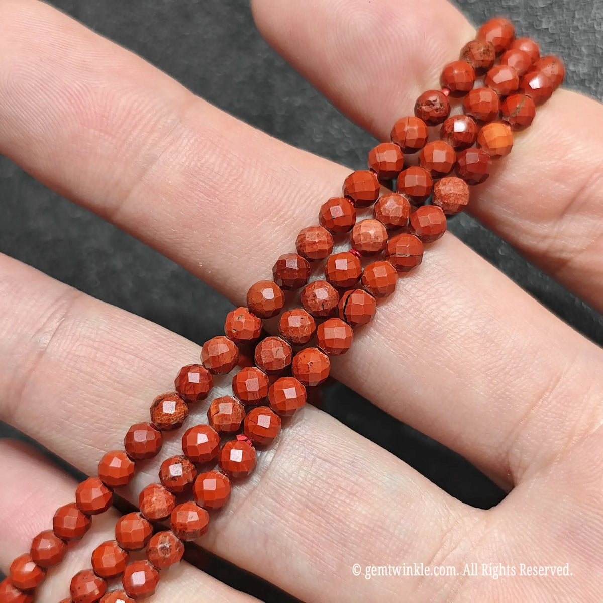 Trio of natural undyed red jasper faceted micro bead bracelets stacked across hand demonstrating dainty everyday layering