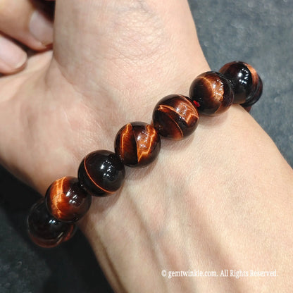 Hand worn perspective of a 12mm red tiger's eye stretch bracelet under ambient illumination