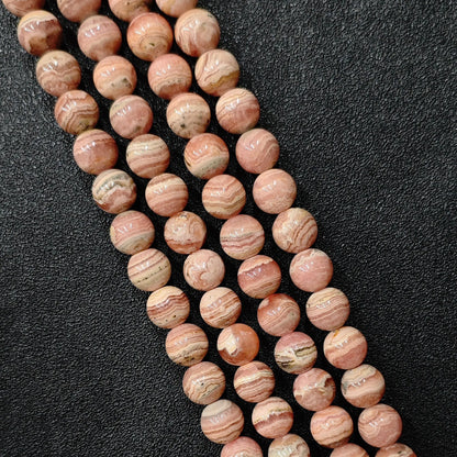 Natural rhodochrosite crystal beads showing beautiful banded pink and cream white stripe patterns in loose strands