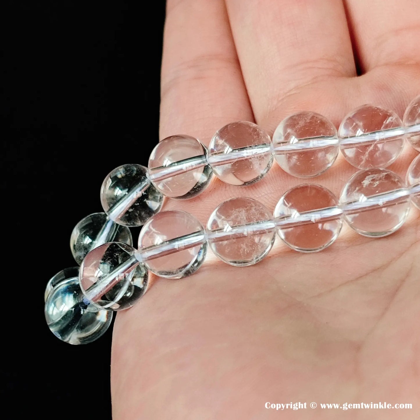 Two strands of natural rock crystal quartz loose round beads drape over a hand, illustrating how subtle inclusions become slightly more defined in larger bead sizes