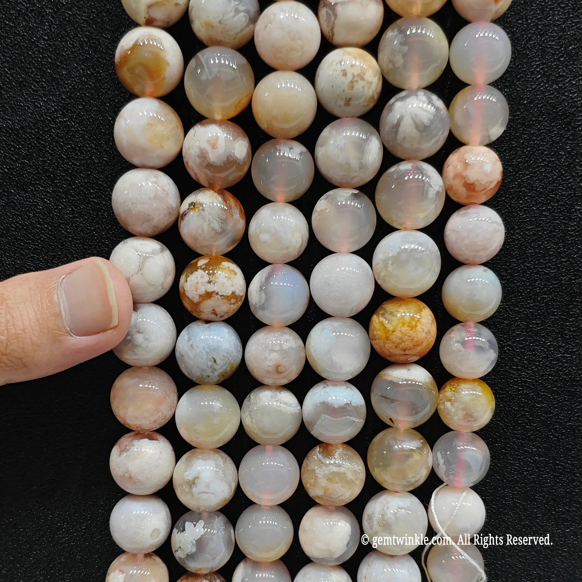 Inspecting a premium bundle of natural sakura agate round beads from 4mm to 14mm with finger for boutique size grid verification