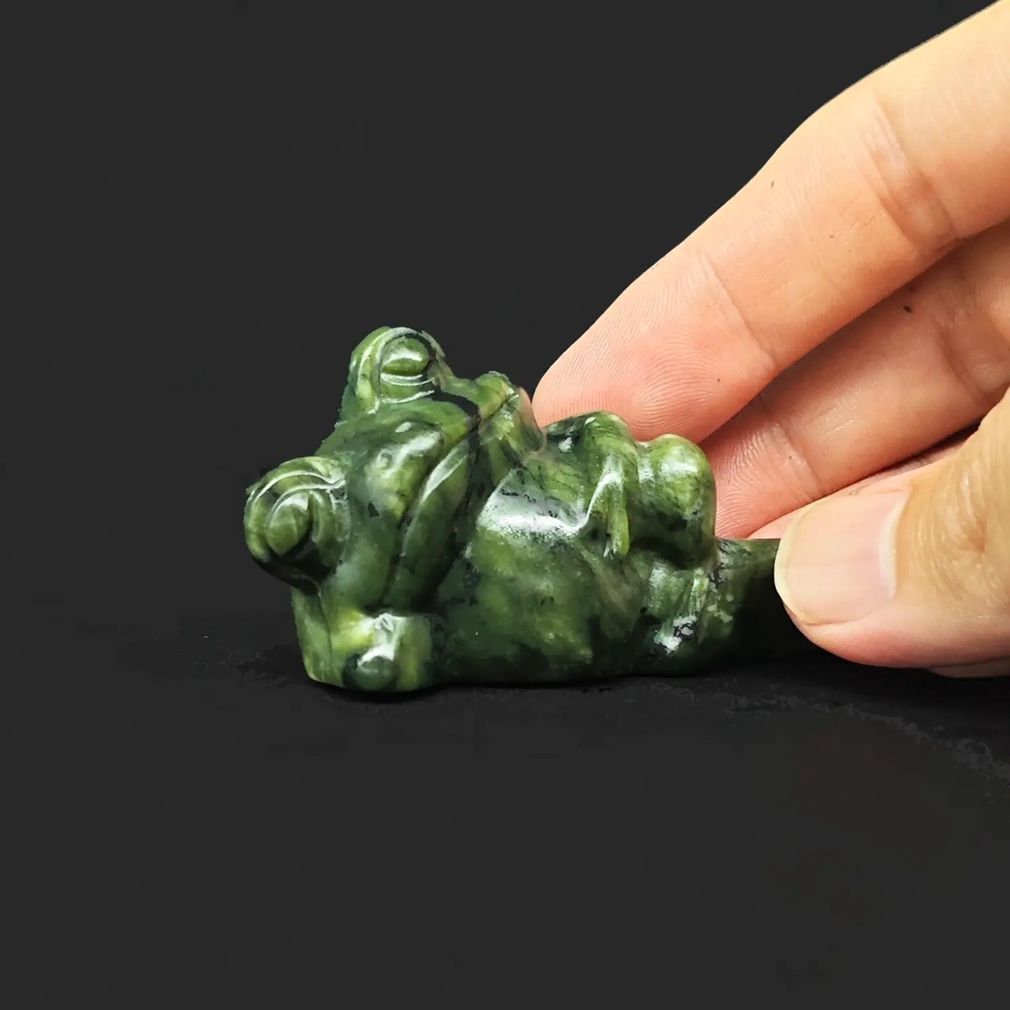 Side close up view of a natural serpentine reclining frog statue showing a funny lazy toad lounging on its side with hand under head