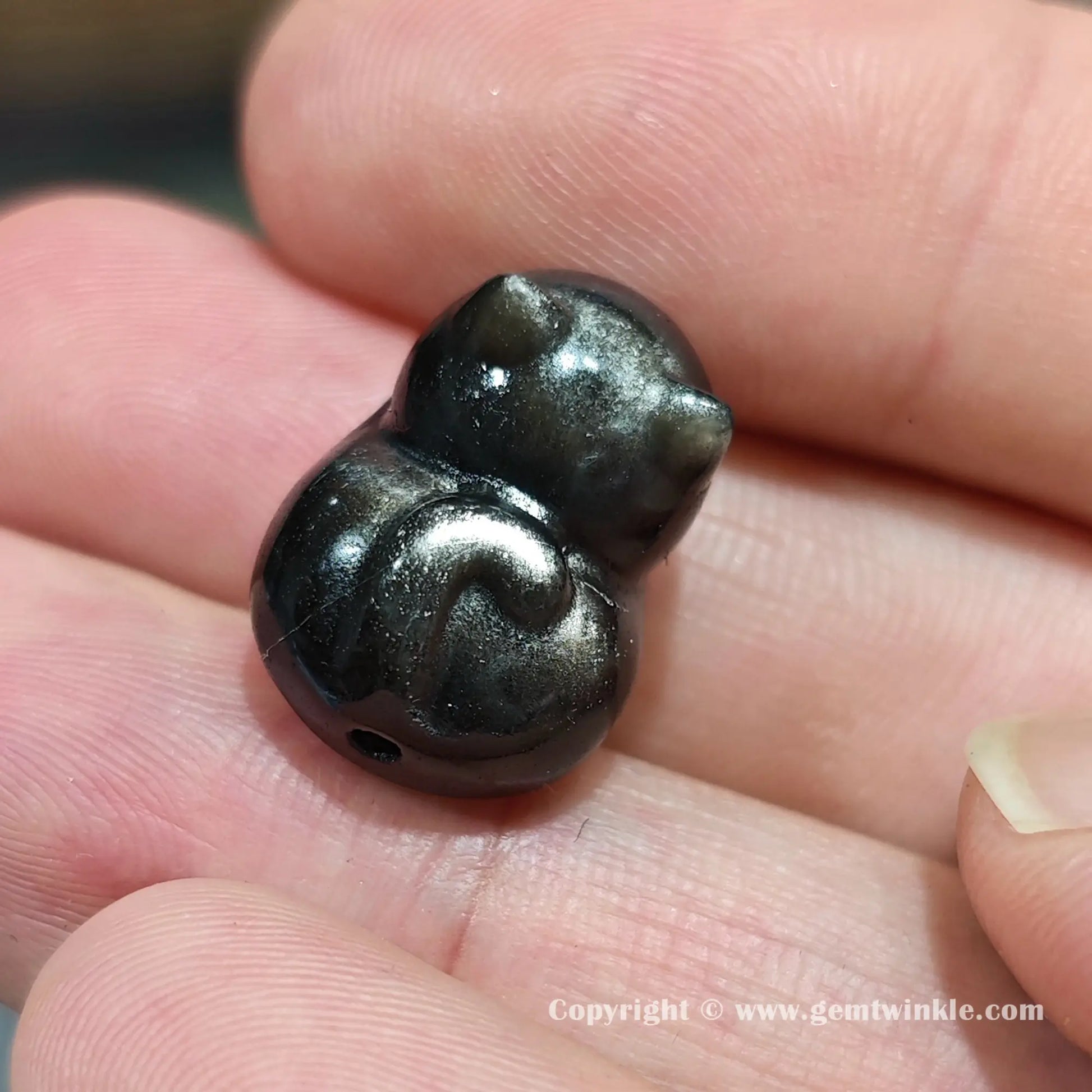 Close up details of silver sheen obsidian cat focal charm bead displaying rich metallic chatoyancy on hand