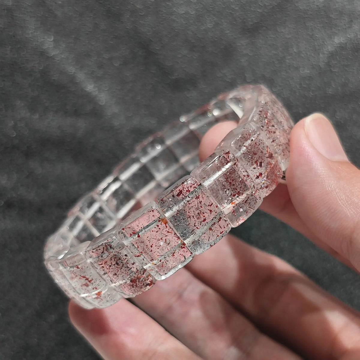 Hand holding a natural strawberry quartz plate bead bracelet showcasing clear quartz matrix filled with red lepidocrocite flakes