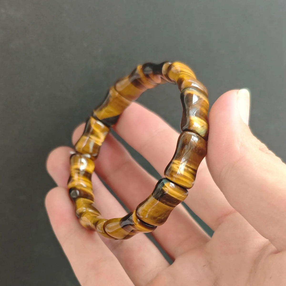 Natural Tiger Eye gemstone bamboo carved tube bead bracelet held on hand displaying chatoyant golden brown luster