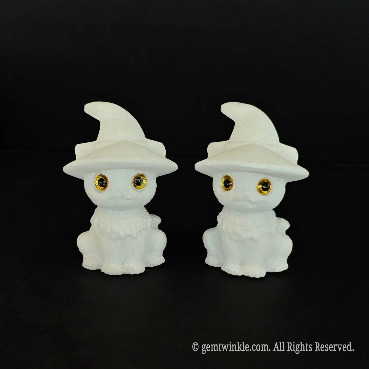 Two 6cm natural white marble cute witch cat figurines with pointed hats and big inlaid amber eyes sitting side by side on a black background