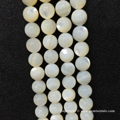Close up view of natural white shell round beads with silky nacre sheen on dark background
