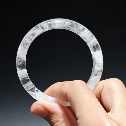 Hand holding a natural white snowflake phantom quartz bangle showing clear icy crystal matrix filled with white mineral phantom inclusions