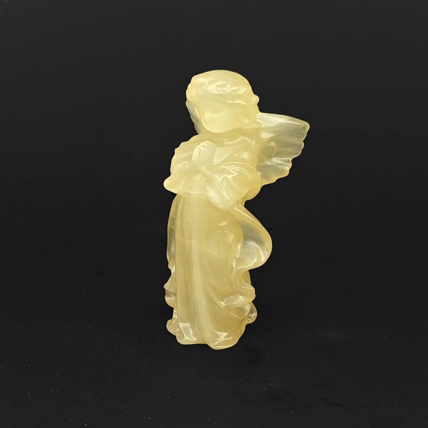 A 10cm hand-carved natural yellow calcite praying guardian angel statue with a translucent honey glow on a dark background for desk decor
