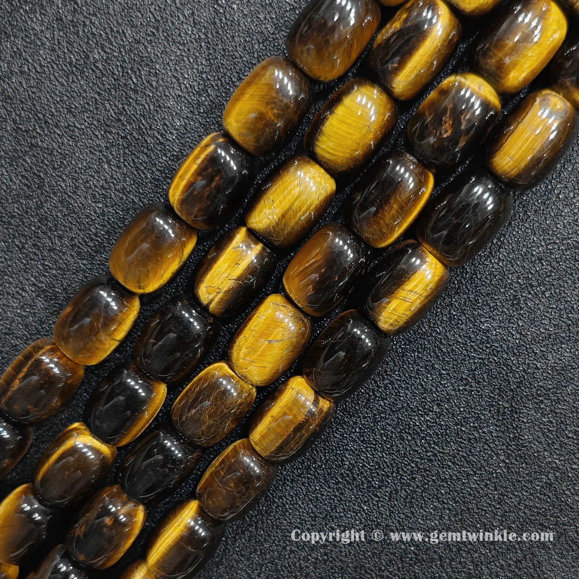 Angled view of smooth polished yellow tigers eye barrel cut gemstone strands