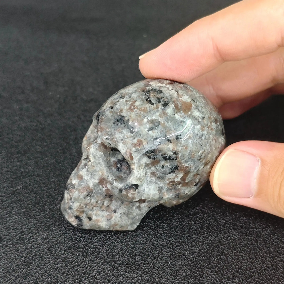 Hand holding a 5cm natural yooperlite crystal skull carving displaying natural grey syenite rock texture in ambient daylight