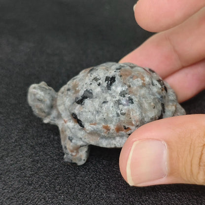 Hand holding a 5cm natural yooperlite turtle carving displaying natural grey syenite rock texture in ambient daylight