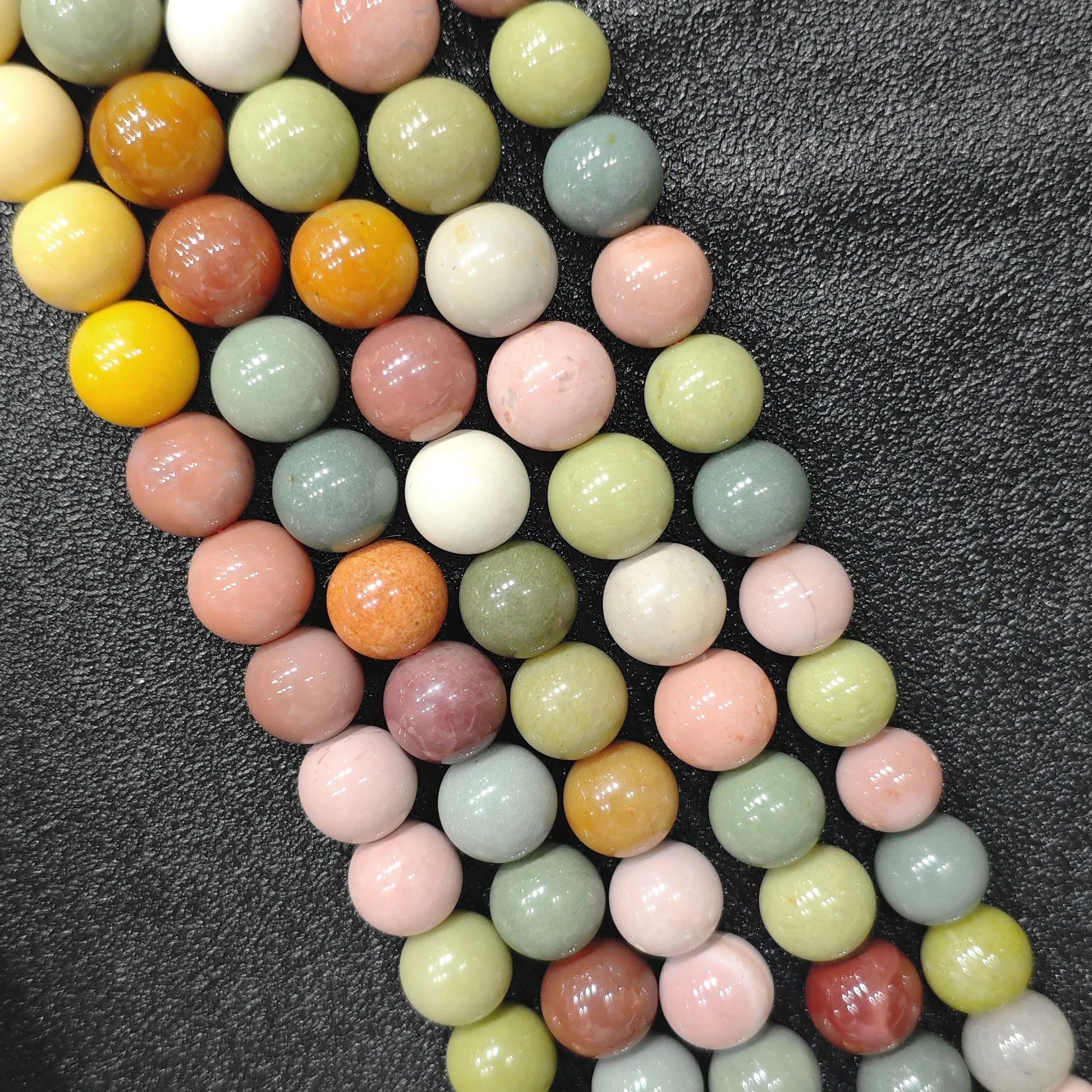 Close up view of natural multicolor Alashan Gobi agate round loose beads on strands displaying yellow green pink and orange hues