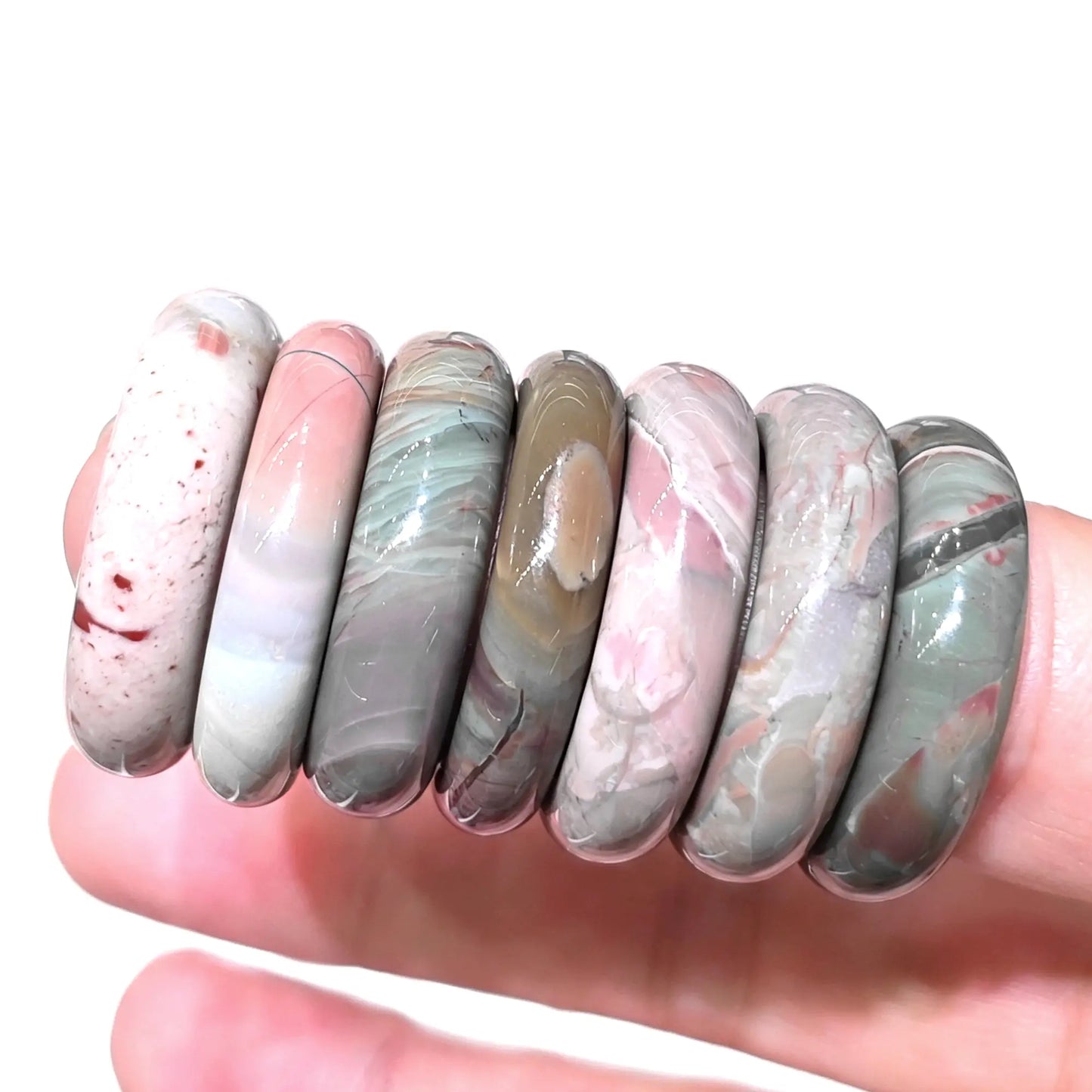 Multiple natural Alashan Gobi agate solid ring bands lined up on hand displaying varied earthy color tones and smooth polish