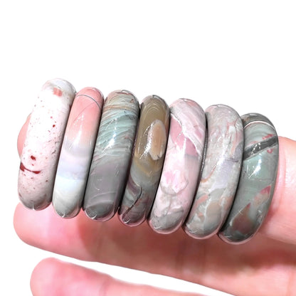 Multiple natural Alashan Gobi agate solid ring bands lined up on hand displaying varied earthy color tones and smooth polish