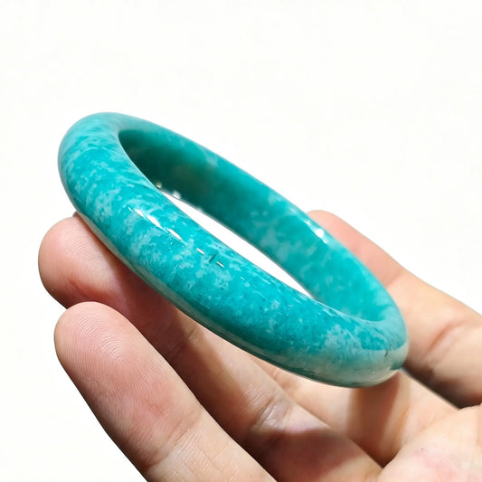 Hand holding a natural turquoise blue amazonite bangle showing white feldspar lattice patterns