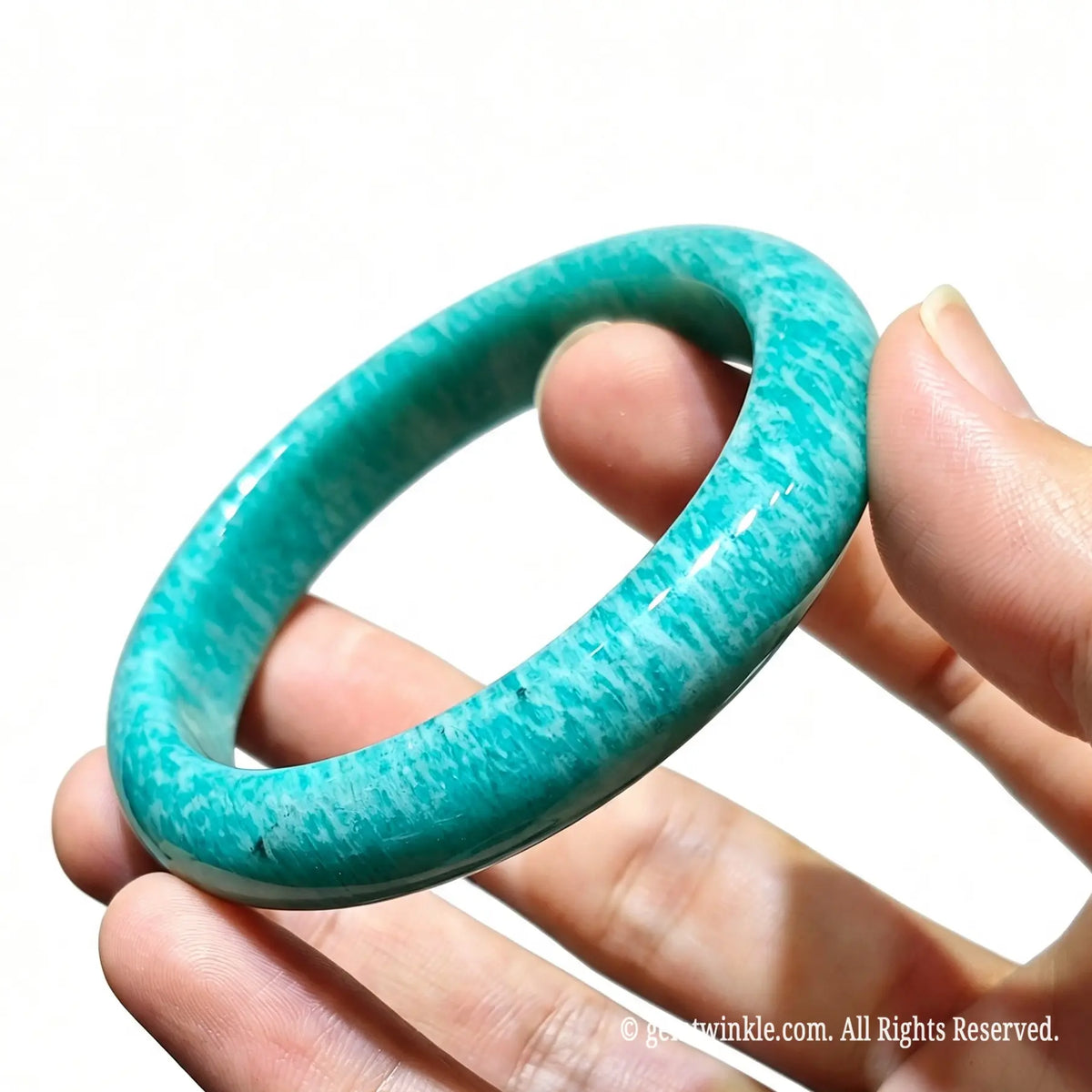 Hand holding a pair of polished natural amazonite bangles showing smooth rounded edge craftsmanship