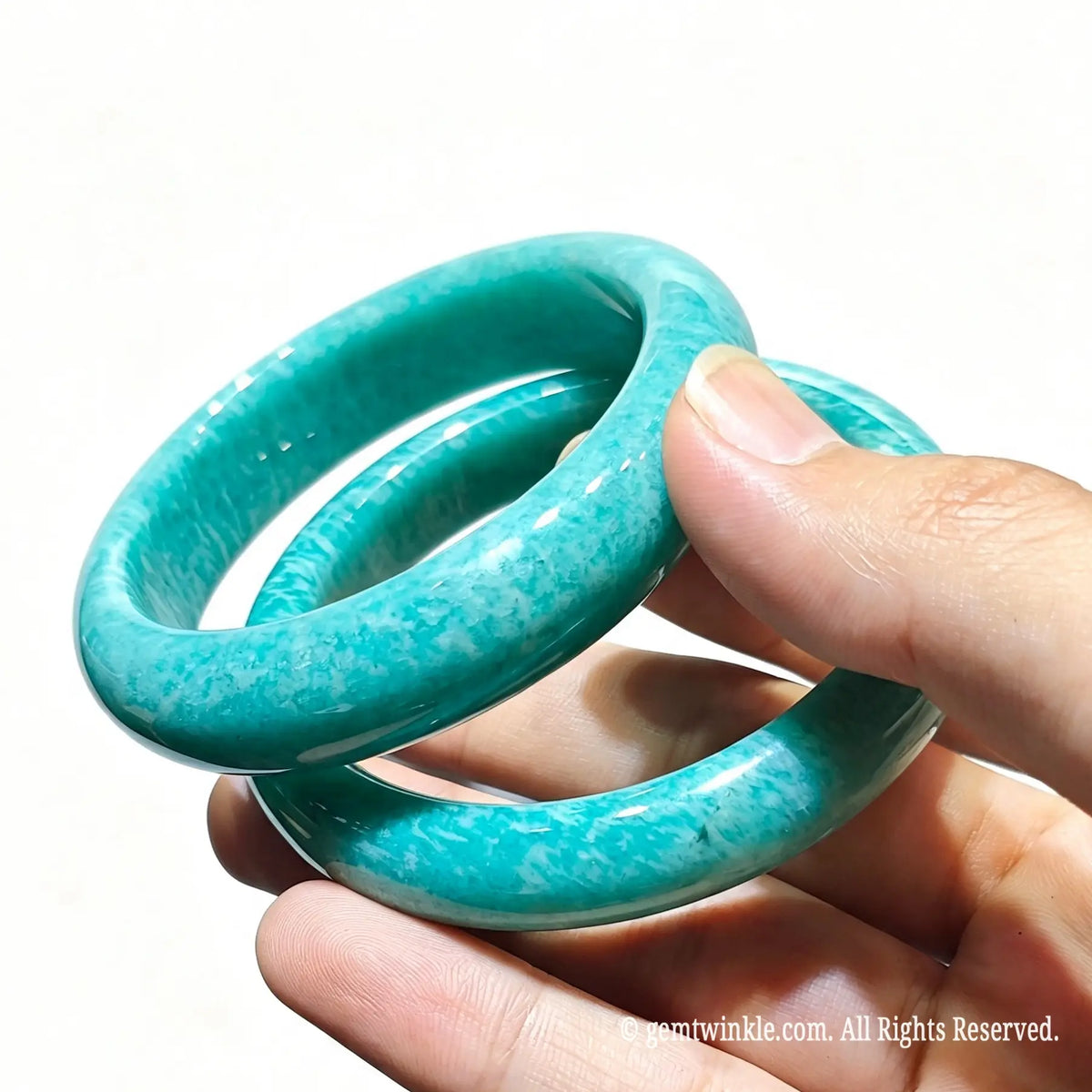 Pair of natural blue green amazonite bangles held in hand showcasing rich seafoam tones