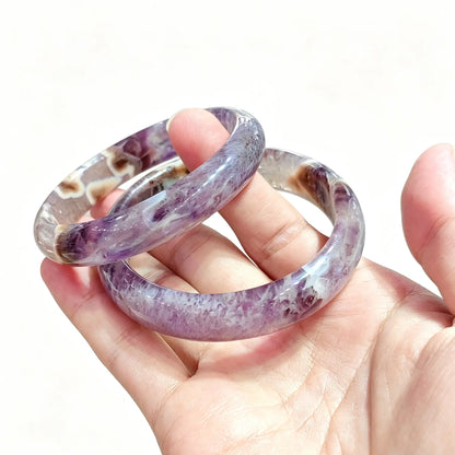 Hand holding a pair of natural amethyst agate bangles showcasing purple crystal matrix and white agate banding