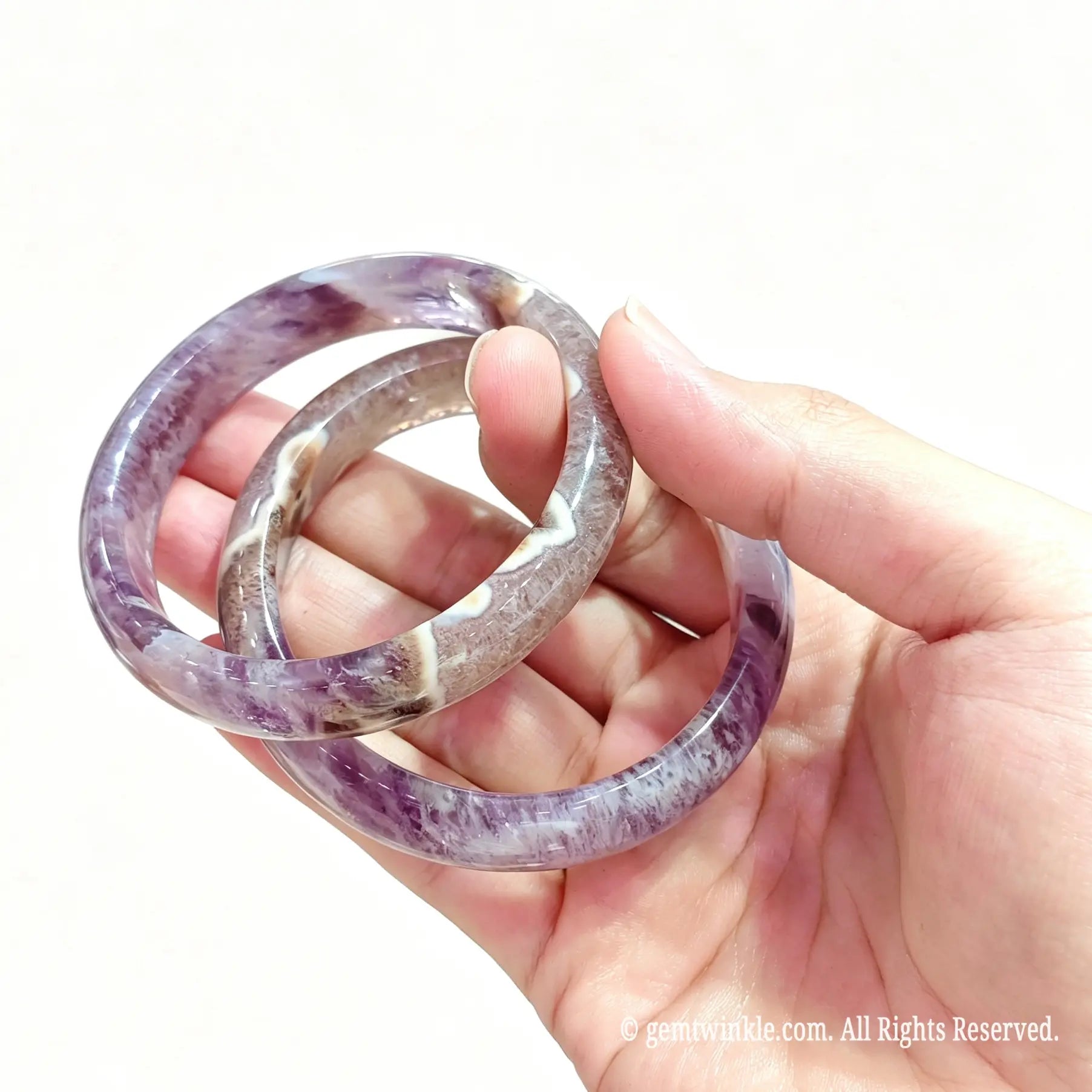 Hand displaying a pair of polished natural amethyst agate bangles for small shop inventory