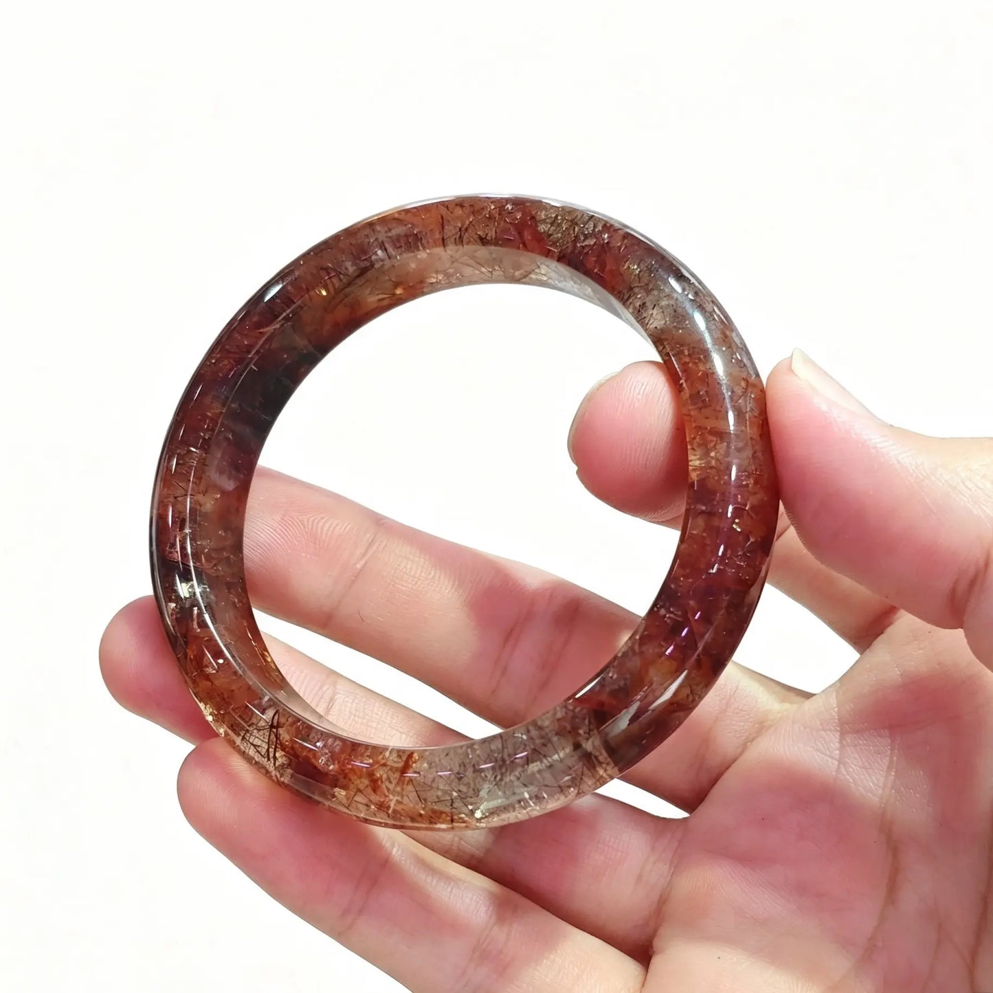 Fingers holding a smooth solid natural black gold super seven quartz bangle showing dense red and dark metallic inclusions