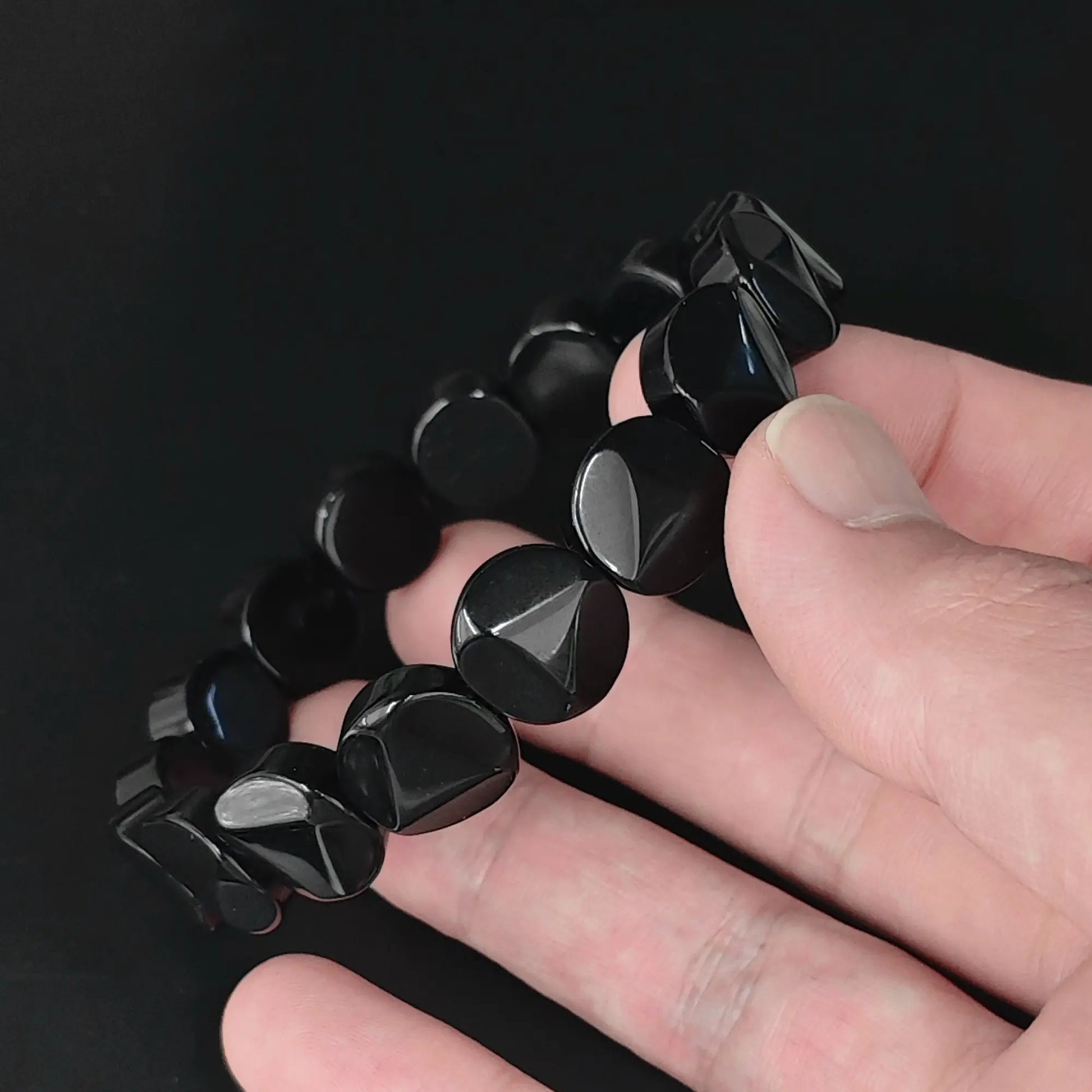 Natural black obsidian 12mm triangle faceted flat round disc bead bracelet held in hand showing raised central triangle facets