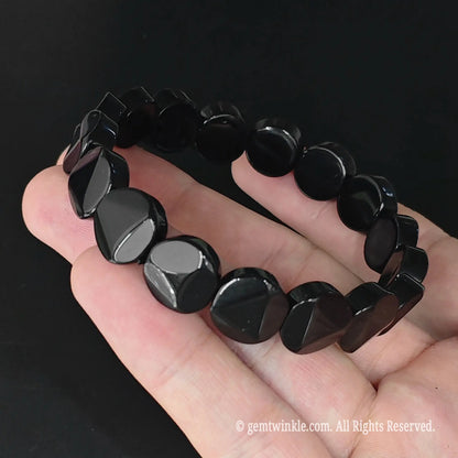 Side angle view of natural black obsidian flat round disc bracelet highlighting polished disc edges and center facet height