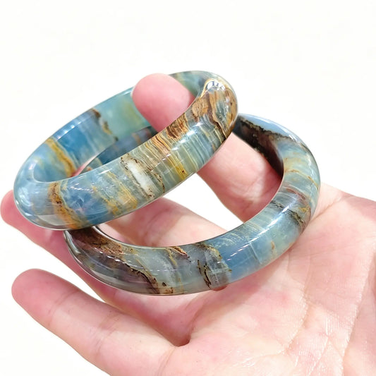 Hand holding a pair of natural blue calcite bangles showcasing sky-blue tones and brown matrix banding