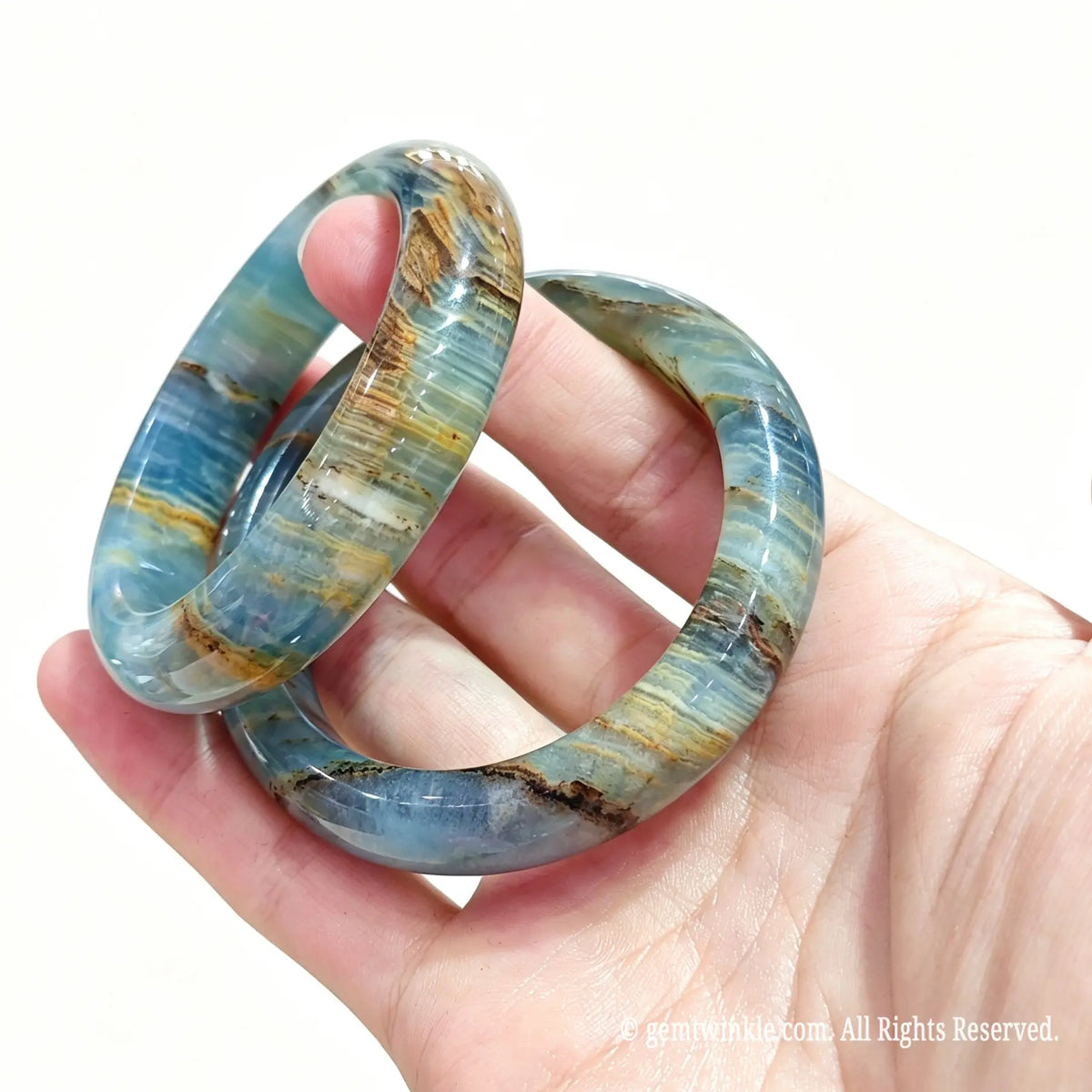 Hand displaying a pair of polished natural blue calcite bangles for small shop inventory