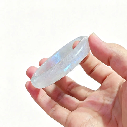 Hand holding a natural blue flash moonstone bangle showcasing glowing blue adularescence on icy matrix