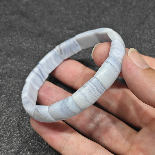 natural blue lace agate curved tile bracelet held between fingers showing soft sky blue and white wavy agate banding