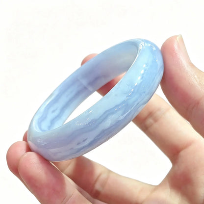 Fingers holding a smooth solid natural blue lace agate bangle displaying pastel sky blue banding and translucent luster
