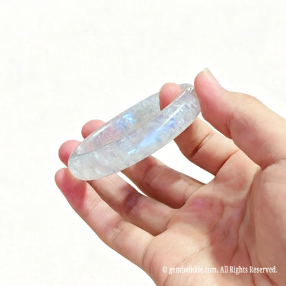 Hand displaying a pair of polished natural blue flash moonstone bangles for small shop inventory