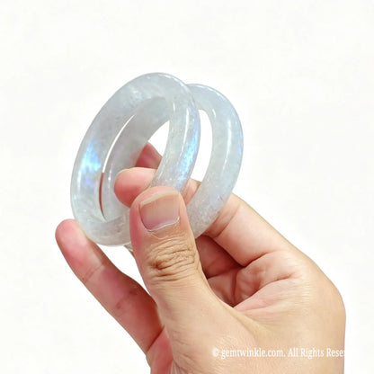 Pair of translucent blue sheen moonstone bangles held in hand showing smooth polish and internal veil