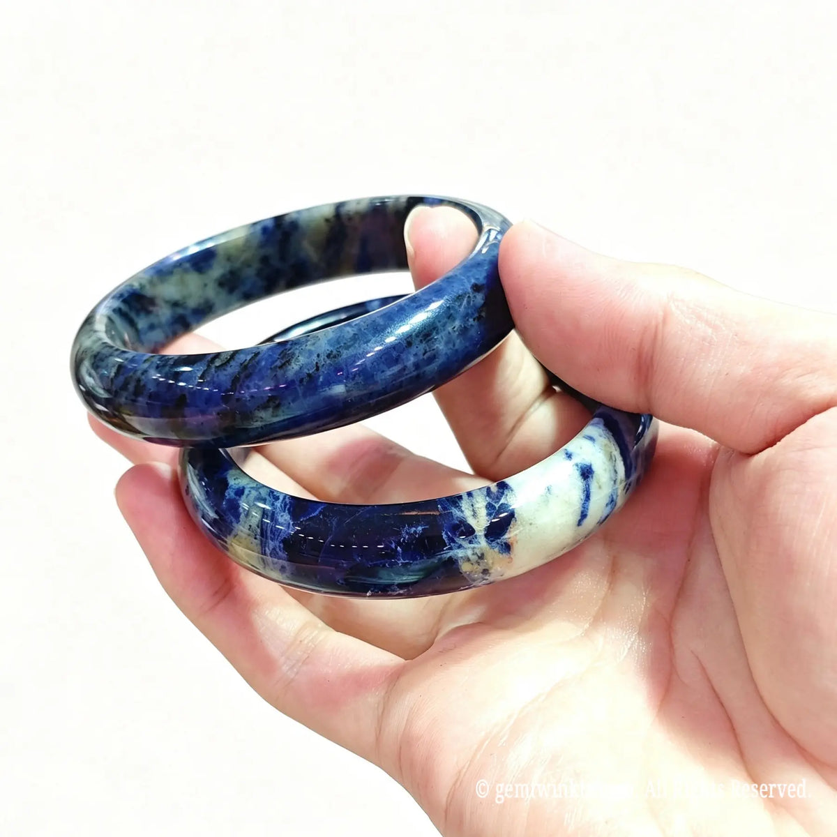 Pair of natural sodalite bangles held in hand showing denim blue mineral texture and smooth rounded polish