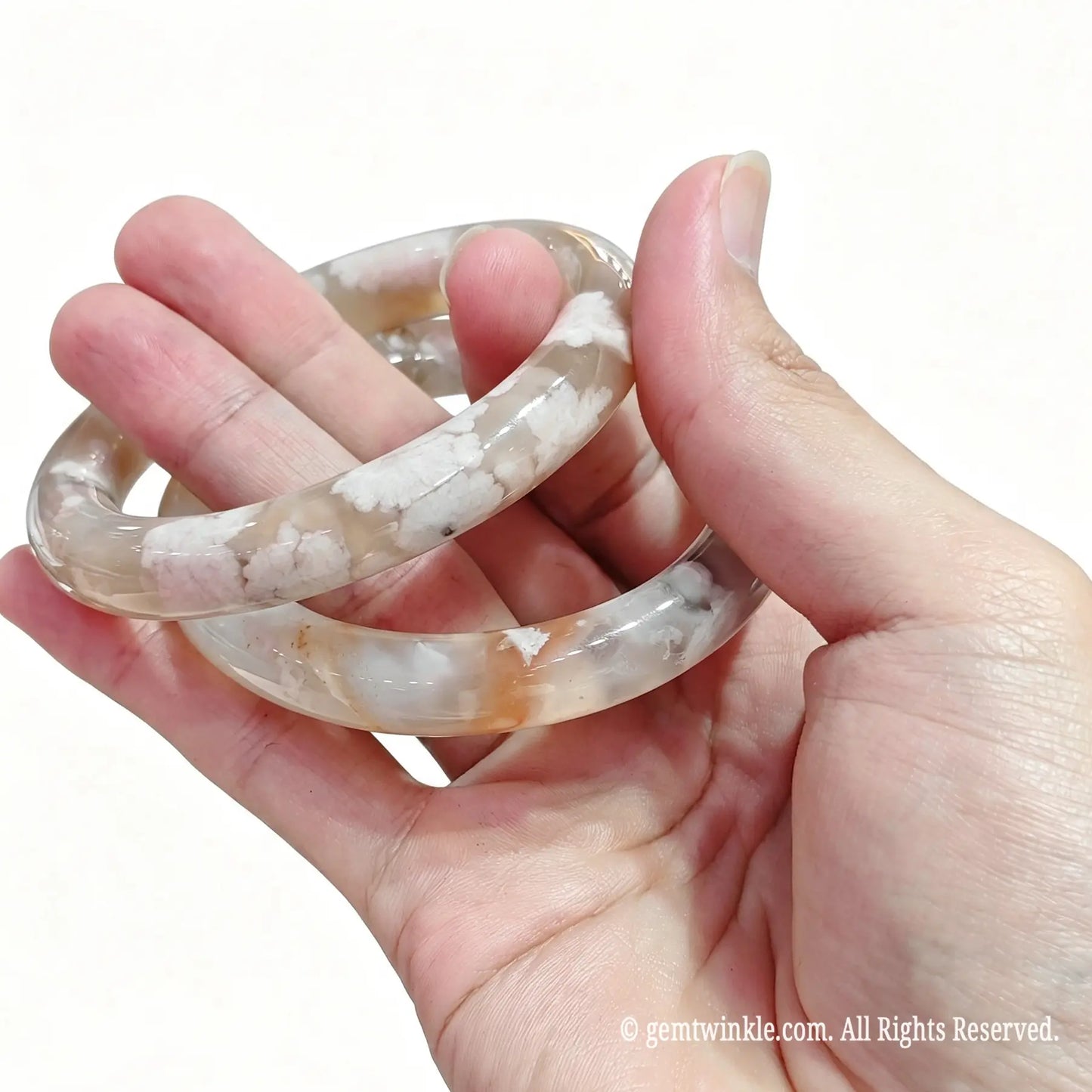 Pair of translucent flower agate bangles held in hand showing smooth rounded polish and white petaled patterns
