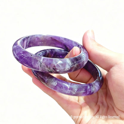 Pair of natural dream amethyst bangles held in hand displaying rich violet tone and smooth rounded polish