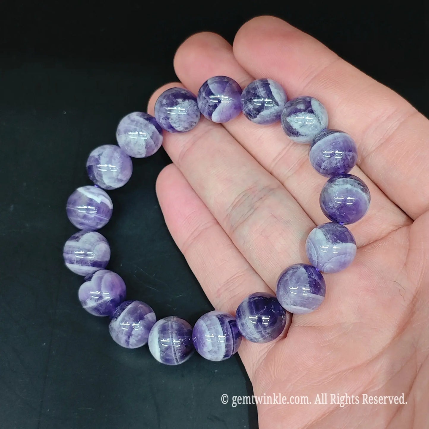 Full view of natural chevron amethyst round bead stretch bracelet resting open on hand showcasing distinct quartz patterns