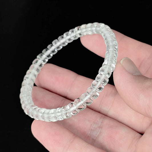Natural clear quartz 5.5-6mm straight cut wheel bead bracelet held in hand showing translucent clarity with natural ice fractures