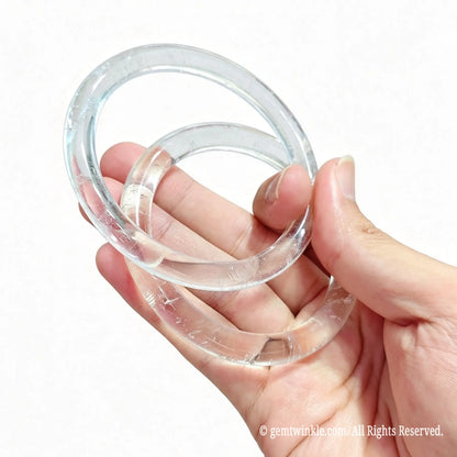 Hand displaying a pair of polished natural clear quartz slim bangles for small shop inventory