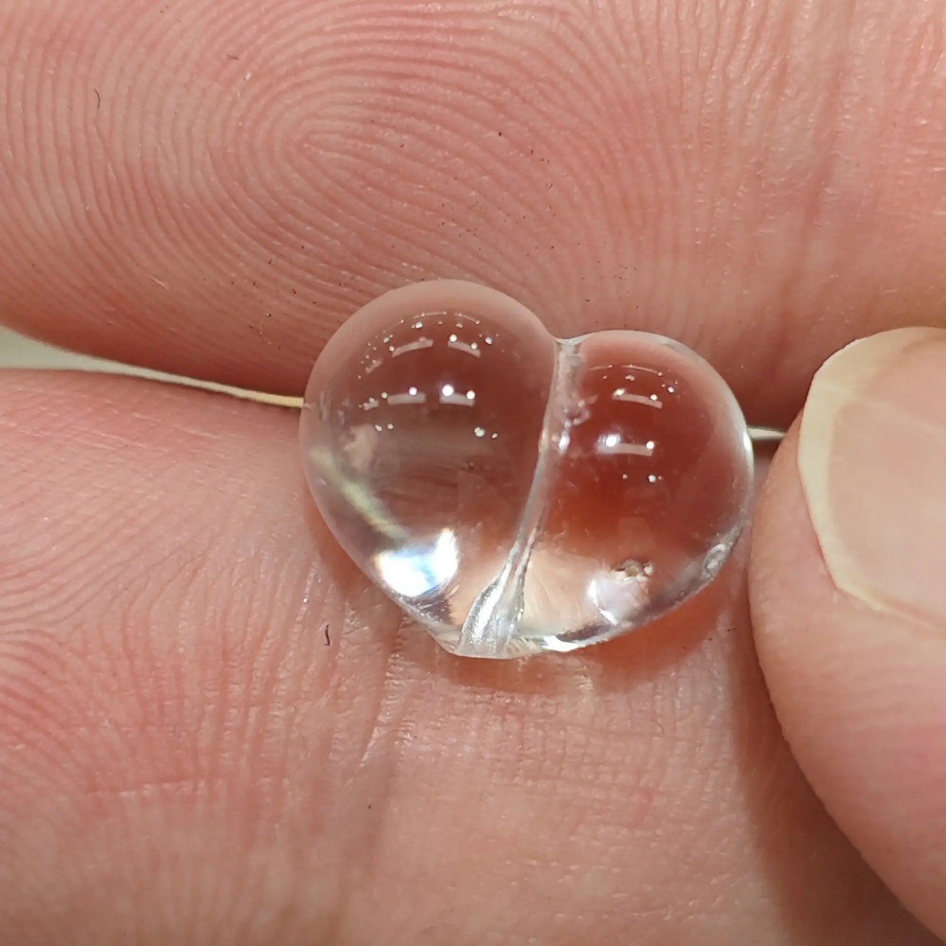 Natural clear quartz carved puffy heart bead vertical drilled close up held in hand showing high clarity transparent crystal